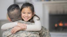 A person wearing military fatigues hugs a child.