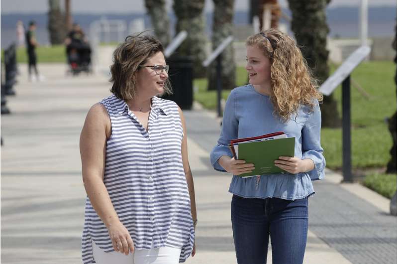 In this Friday, April 10, 2020 photo, Ebru Ural, left, and her daughter Serra Sowers take a walk to discuss choosing colleges without actually visiting them at a park in Sanford, Fla. The coronavirus pandemic has changed the process of college visits to virtual interviews and visits. (AP Photo/John Raoux) Pandemic's toll shows up on students' college applications