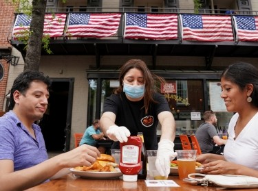 As phase one of reopening begins in Northern Virginia, a waitress with a face mask serves diners at a restaurant in Alexandria, Virginia, May 29, 2020, photo by Kevin Lamarque/Reuters