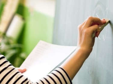 Teacher writing on a blackboard, photo by Andrea Obzerova/Adobe Stock