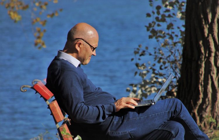 older man sitting on park bench with laptop