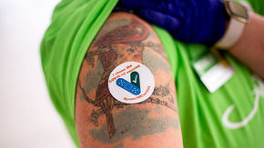 an individual shows off a sticker on their upper arm. The sticker reads “I chose the COVID-19 vaccine.”