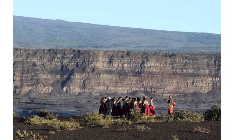 In this April 25, 2019, photo, a group of Native Hawaiians stand next to the collapsed caldera floor of Kilauea volcano in Hawaii Volcanoes National Park on the Big Island. The U.S. Geological Survey says the Kilauea volcano on Hawaii's Big Island has erupted. The eruption began late Sunday, Dec. 20, 2020 within the Halema'uma'u crater. The volcano is located within Hawaii Volcanoes National Park. (AP Photo/Caleb Jones, File) Volcano erupts on Hawaii's Big Island, draws crowds to park