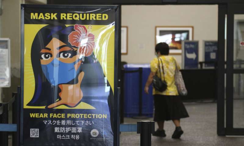 In this Oct. 2, 2020 file photo, a woman walks into the international airport in Honolulu amid a quarantine rule that effectively shut down the tourism industry in the state. The small, tight-knit community of about 72,000 people on the neighboring island of Kauai spent the first seven months of the pandemic mostly COVID-free. Then in October, statewide travel restrictions eased and the island, which had only 61 known cases of coronavirus from March through September, went from zero cases in October to at least 84 new infections in just seven weeks. (AP Photo/Caleb Jones, File) Mostly virus-free Kauai hit by pandemic after travel resumes