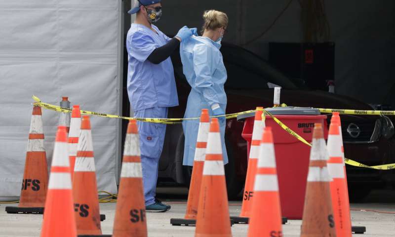 In this July 5, 2020, file photo, healthcare workers help each other with their personal protective equipment at a drive-thru coronavirus testing site outside Hard Rock Stadium in Miami Gardens, Fla. The PPE that was in dangerously short supply during the initial weeks of the coronavirus crisis in the U.S. is running out again as the virus resumes its rapid spread and the number of hospitalized patients climbs. (AP Photo/Wilfredo Lee, File) Protective gear for medical workers begins to run low again