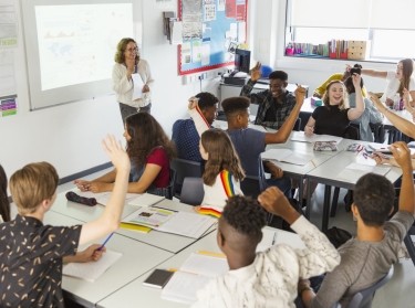High school students with hands raised during lesson in classroom, photo by Chris Ryan/KOTO/AdobeStock