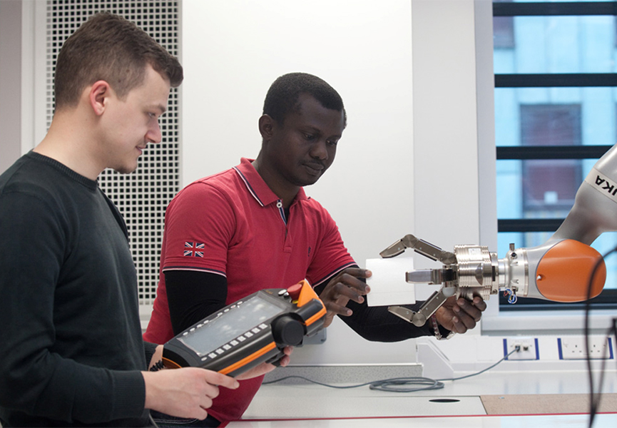 Two apprentices programming a robotic arm