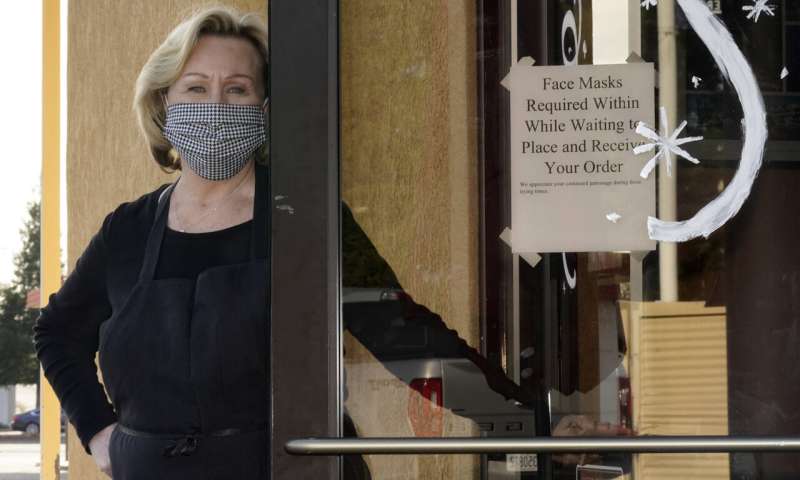 Brenda Luntey, poses for a photo by a sign advising customers to wear face masks that is posted on the door of the San Francisco Deli in Redding, Calif., Thursday, Dec. 3, 2020. Luntey, who owns the deli with her husband, who says she comes from a law enforcement family and is not a rule breaker, is openly violating the state's order to close her restaurant to indoor dining. "I want people to understand we are not thumbing our nose at the government,"said Luntey, "I'm trying to keep my business alive. (AP Photo/Rich Pedroncelli) As virus slams rural California, many still pan restrictions