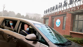 People in a car drive toward the entrance of the Wuhan Institute of Virology