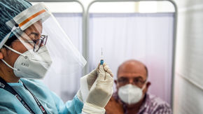 A health care worker wearing personal protective equipment holds a syringe