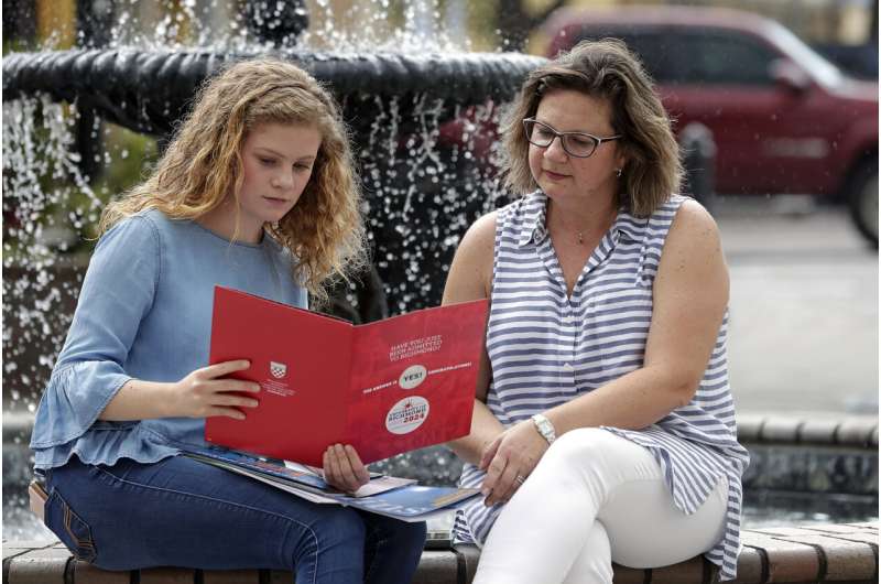 In this Friday, April 10, 2020, photo in Sanford, Fla., Serra Sowers, left, and her mother Ebru Ural look over brochures from various colleges. The coronavirus pandemic has changed the process of college visits to online and virtual interviews. (AP Photo/John Raoux) Pandemic's toll shows up on students' college applications