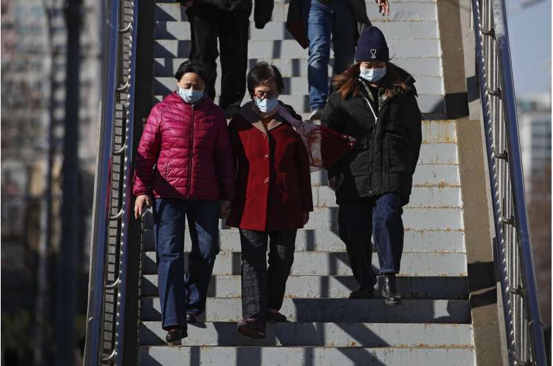People wearing face masks to help curb the spread of the coronavirus walk down a pedestrian overhead bridge in Beijing, Sunday, March 21, 2021. (AP Photo/Andy Wong) China urges unhurried public to get vaccinated against COVID