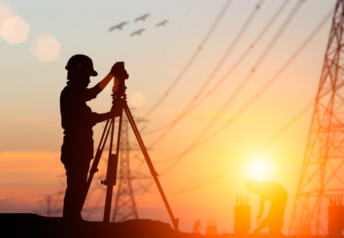 A silhouetted civil engineer surveys the land next to some high voltage transmission lines