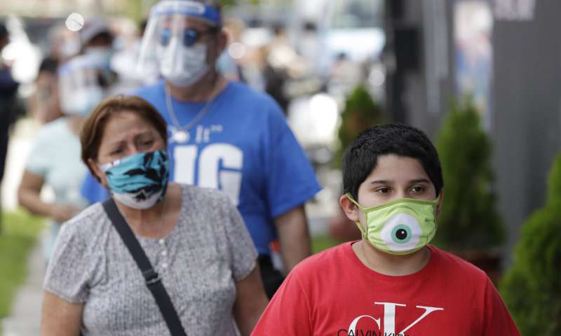 People, social distancing and wearing masks to prevent the spread of the new coronavirus, wait in line at a mask distribution event, Friday, June 26, 2020, in a COVID-19 hotspot of the Little Havana neighborhood of Miami. Florida banned alcohol consumption at its bars Friday as its daily confirmed coronavirus cases neared 9,000, a new record that is almost double the previous mark set just two days ago. (AP Photo/Wilfredo Lee) Germany cautions virus risk still high as economies restart